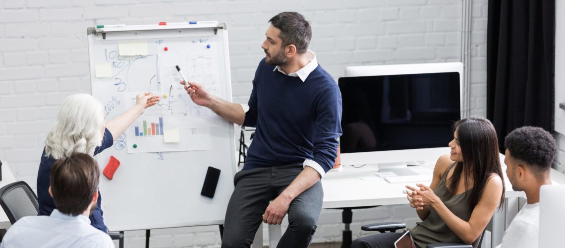 Creative people sitting at table in boardroom with man explaining business strategy